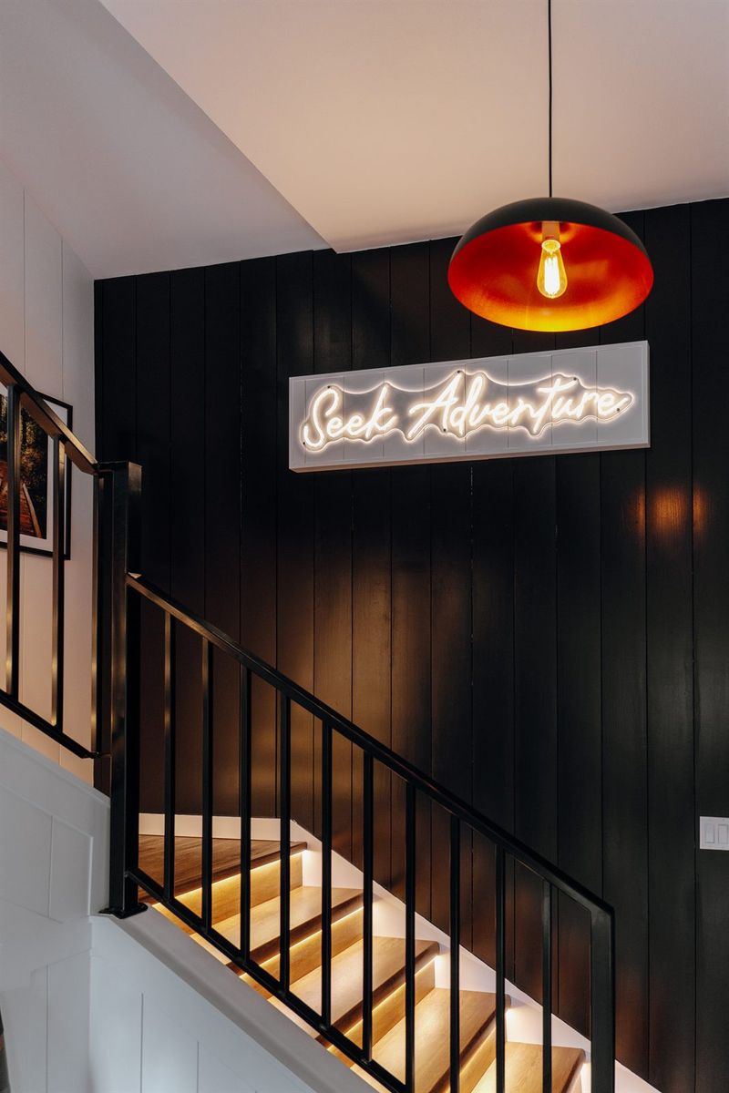 A custom neon "Seek Adventure" sign glowing above the staircase at Timber & Tide.